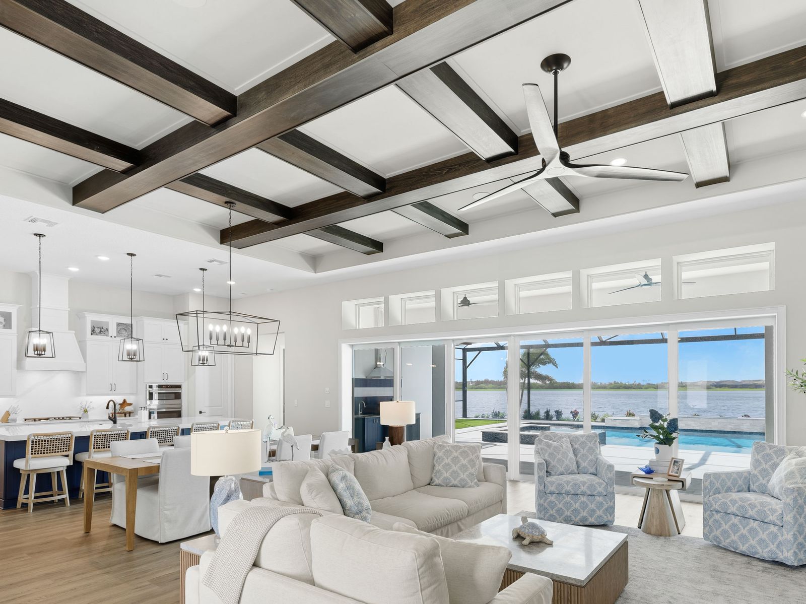 Great room with crossed beams on a white ceiling, open to the kitchen and a lanai with water view