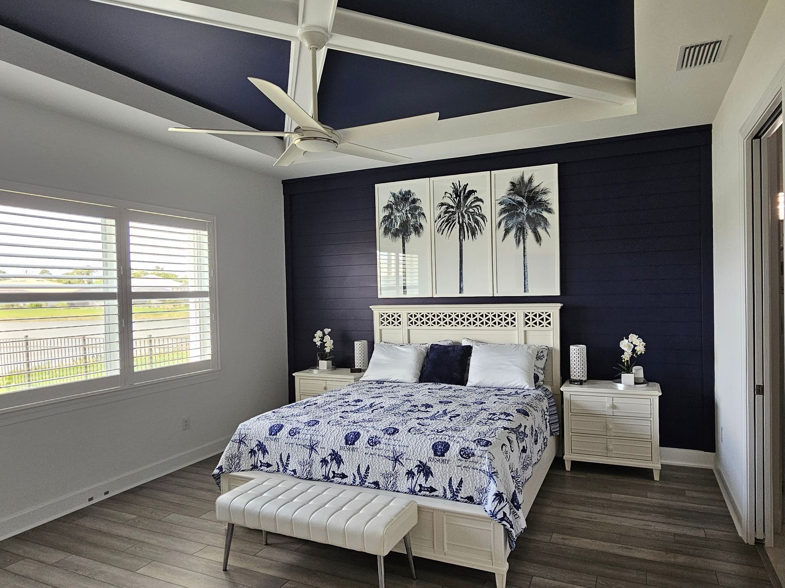 Bedroom with a navy painted ceiling crossed by white beams, a matching navy board wall behind the bed and plantation shutters